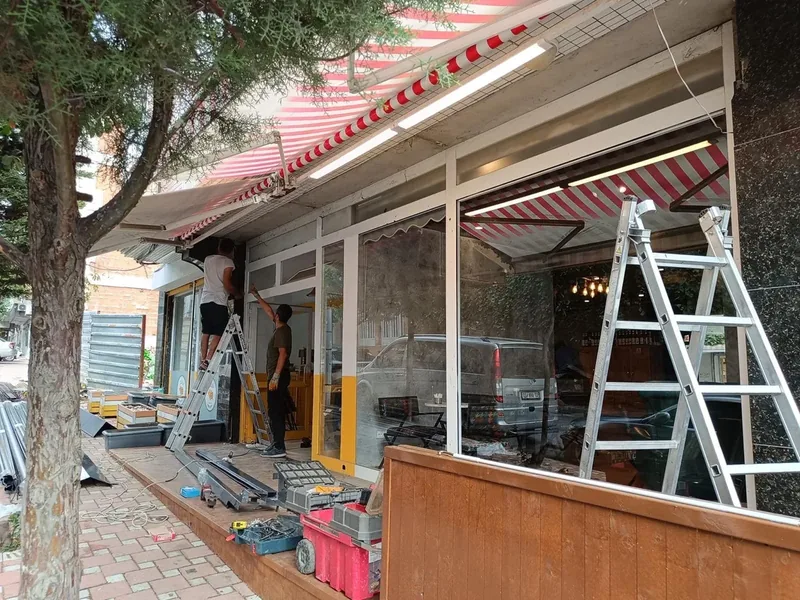 İki usta merdiven üzerinde bir kafe cephesine kepenk takıyor